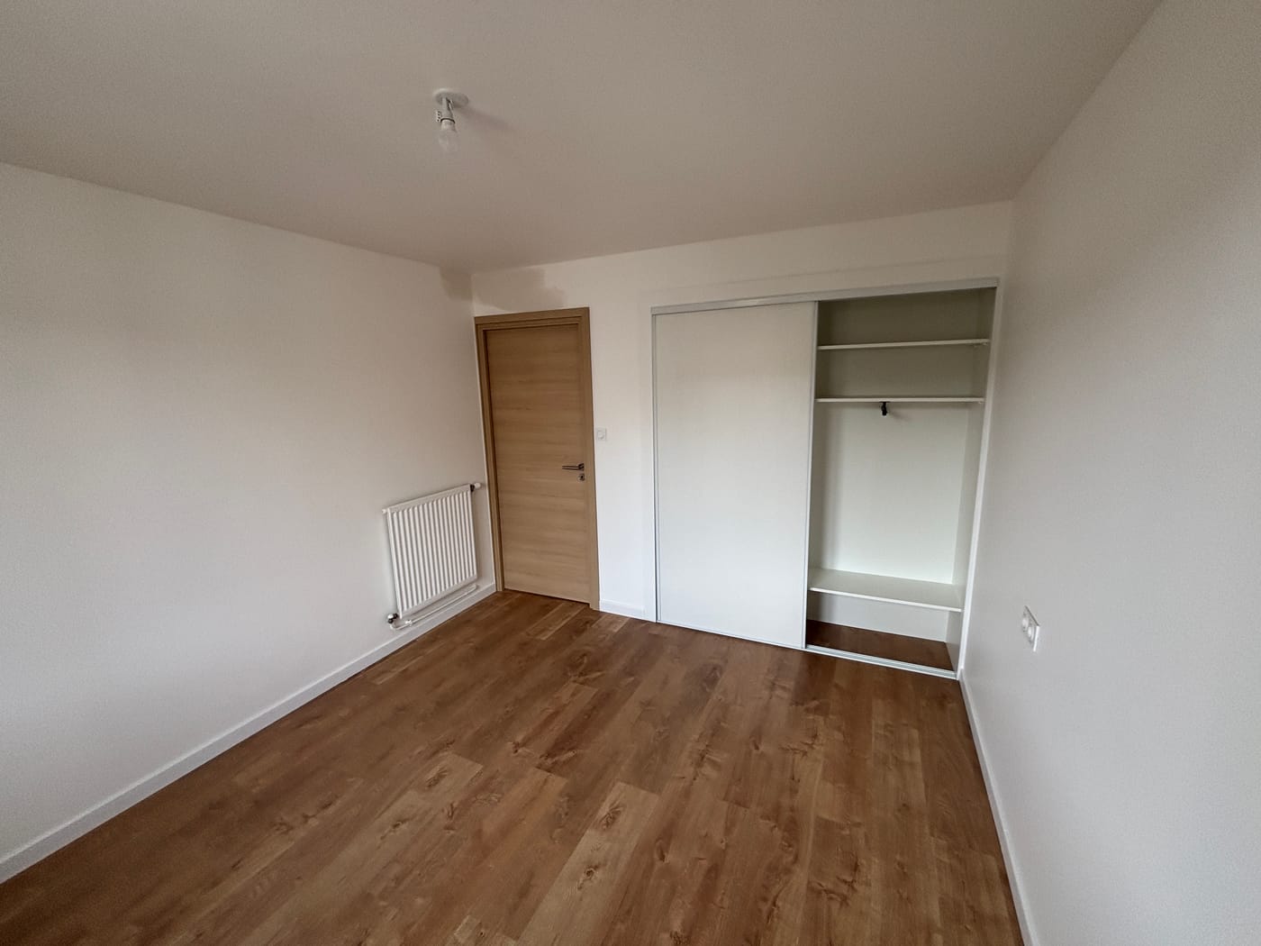 Une chambre après les travaux : sol neuf, murs blancs, porte en chêne clair et placard intégré à portes coulissantes