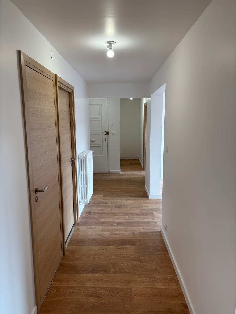 Le couloir de distribution après les travaux : murs clairs, sol aspect bois, portes en chêne clair