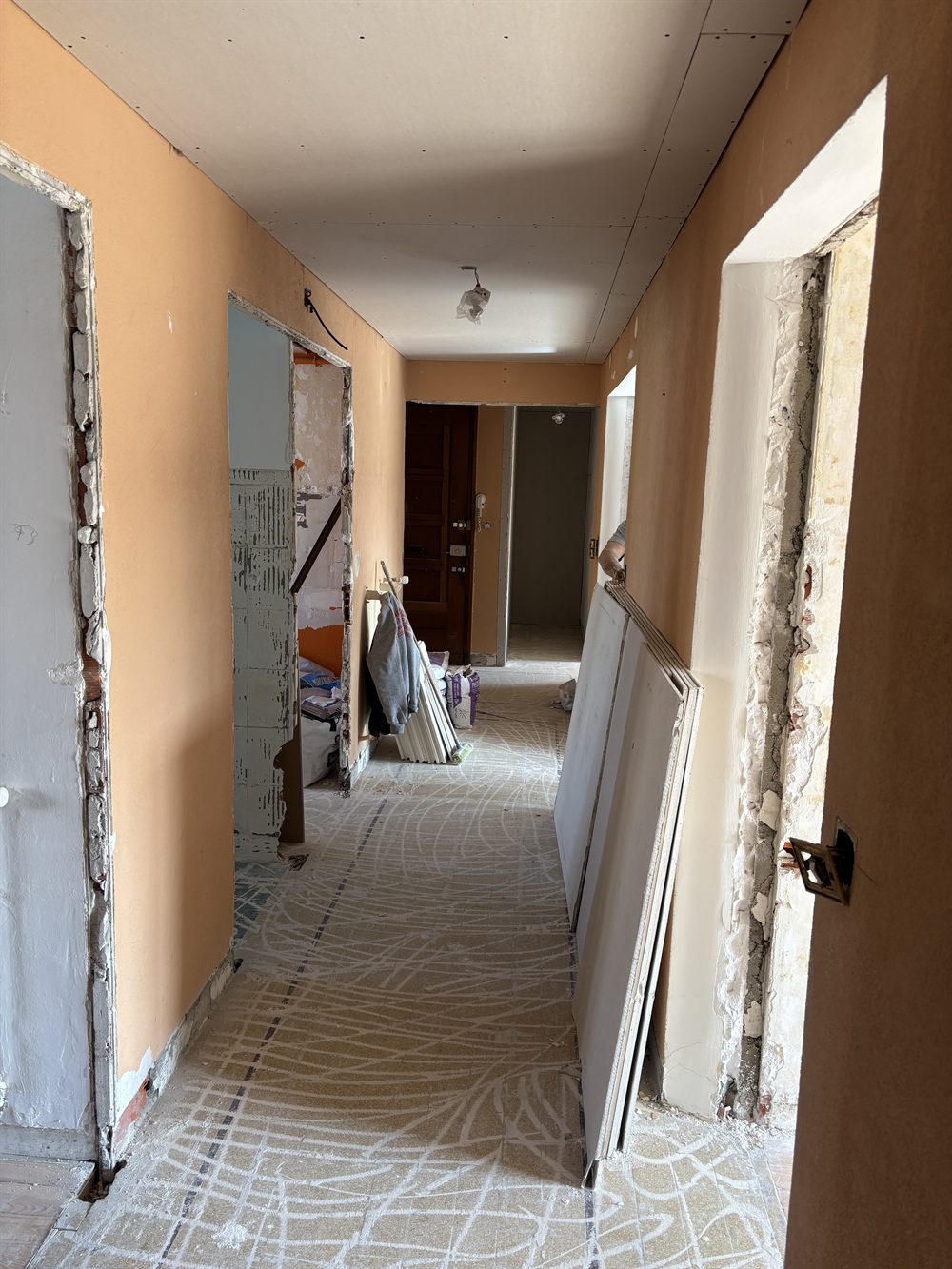 Le couloir pendant les travaux : portes déposées et posées contre le mur, huisseries à nu, traces de colle au sol