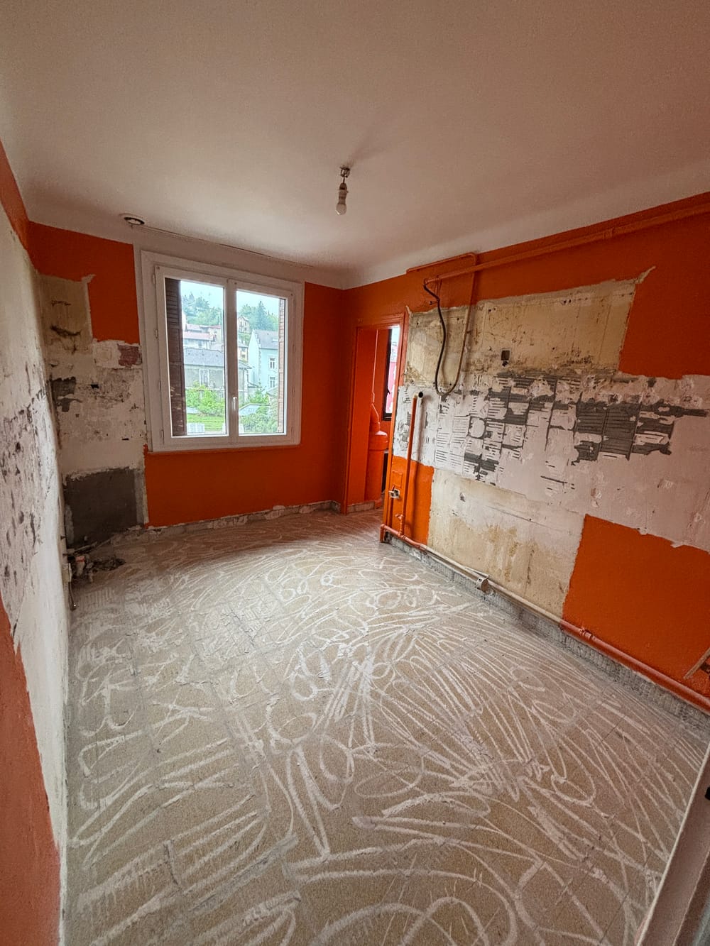 La cuisine pendant les travaux : meubles et faïence déposés, murs mis à nu, traces de colle au sol