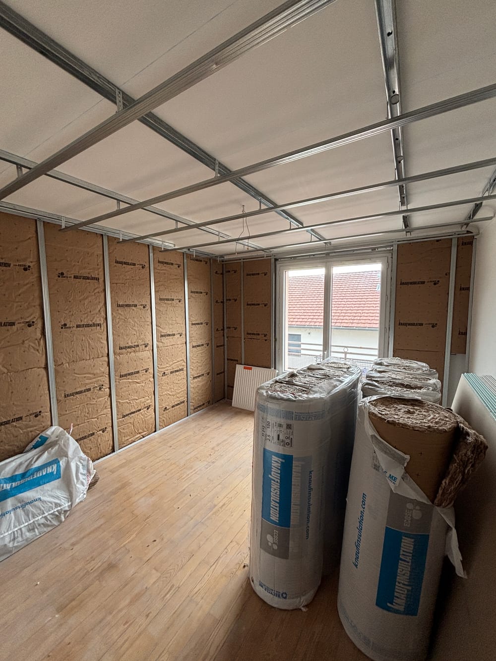 Une pièce en cours de travaux : isolant posé sur les murs, ossature métallique du futur plafond et rouleaux d'isolant en attente