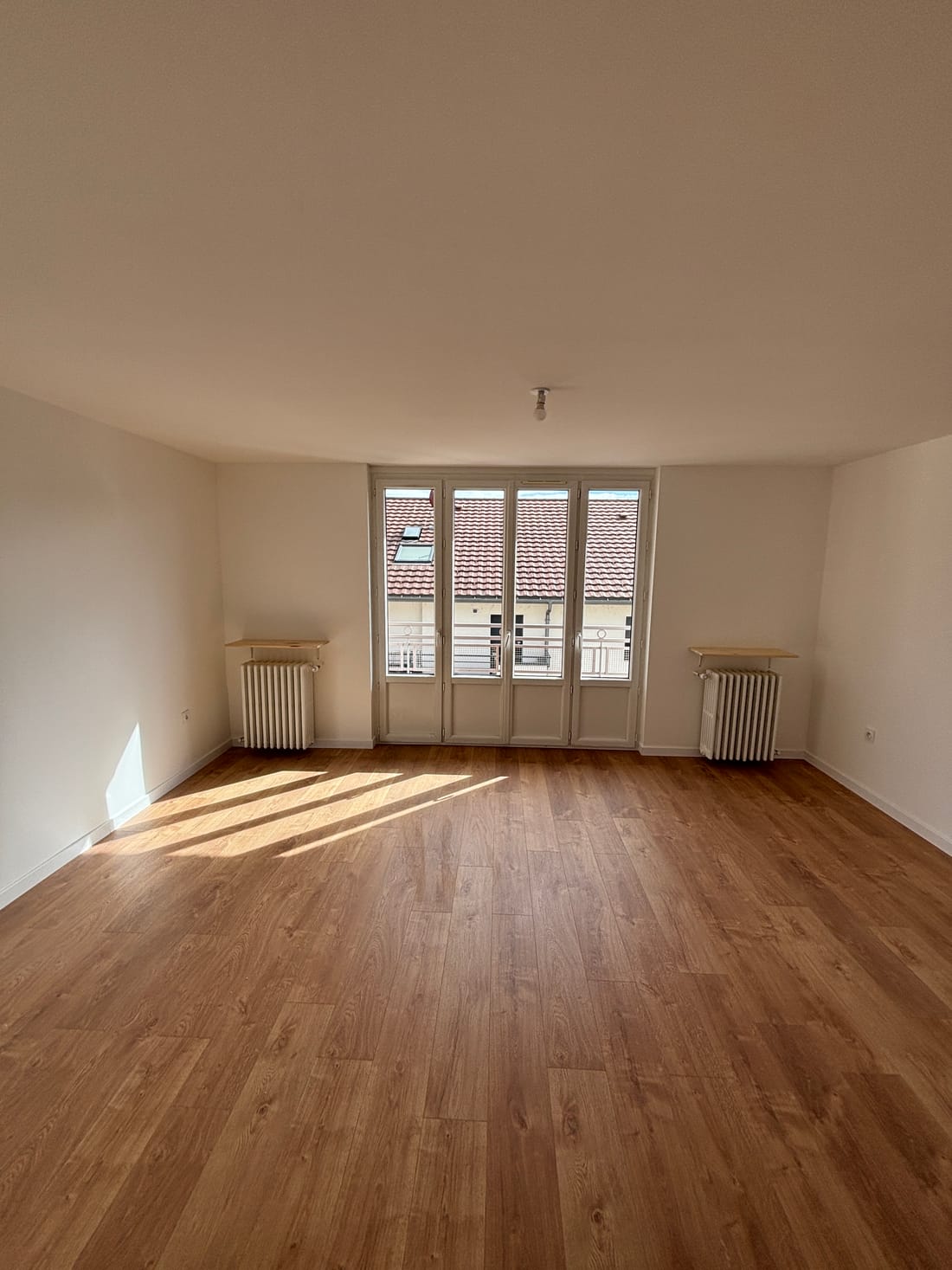 Le séjour après les travaux : sol neuf, murs et plafond blancs, radiateurs en fonte conservés sous tablettes, lumière du jour par la porte-fenêtre
