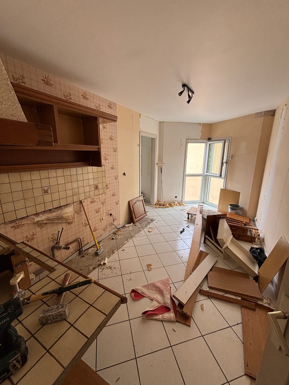 La cuisine pendant les travaux : meubles et faïence en cours de dépose, panneaux de bois et gravats au sol