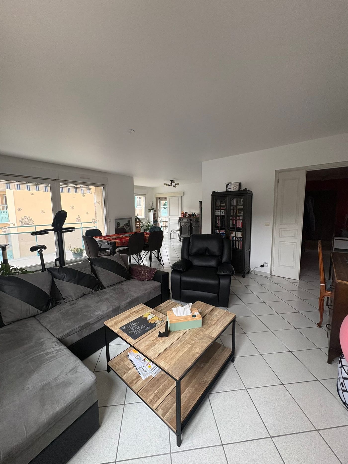Le séjour du projet Le Nautile avant les travaux : carrelage blanc, baie vitrée sur balcon, canapé d'angle et coin repas au fond