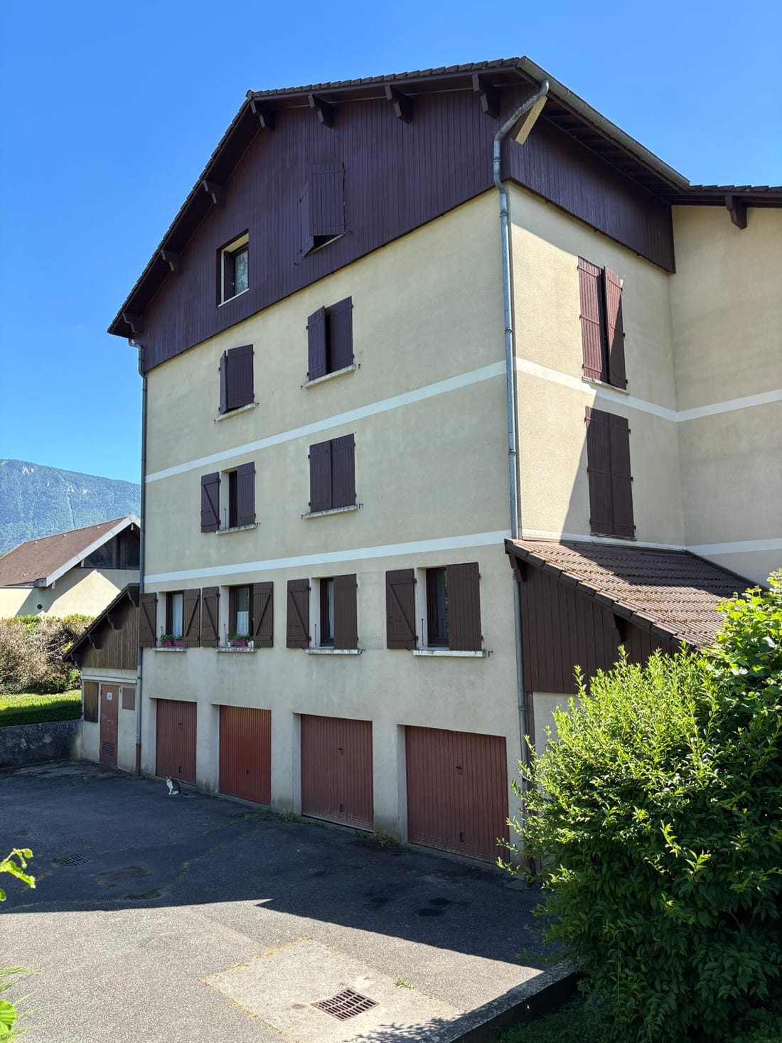 Le bâtiment existant à Yenne, avant travaux : façade claire à volets bruns, bardage bois sous la toiture et garages au rez-de-chaussée